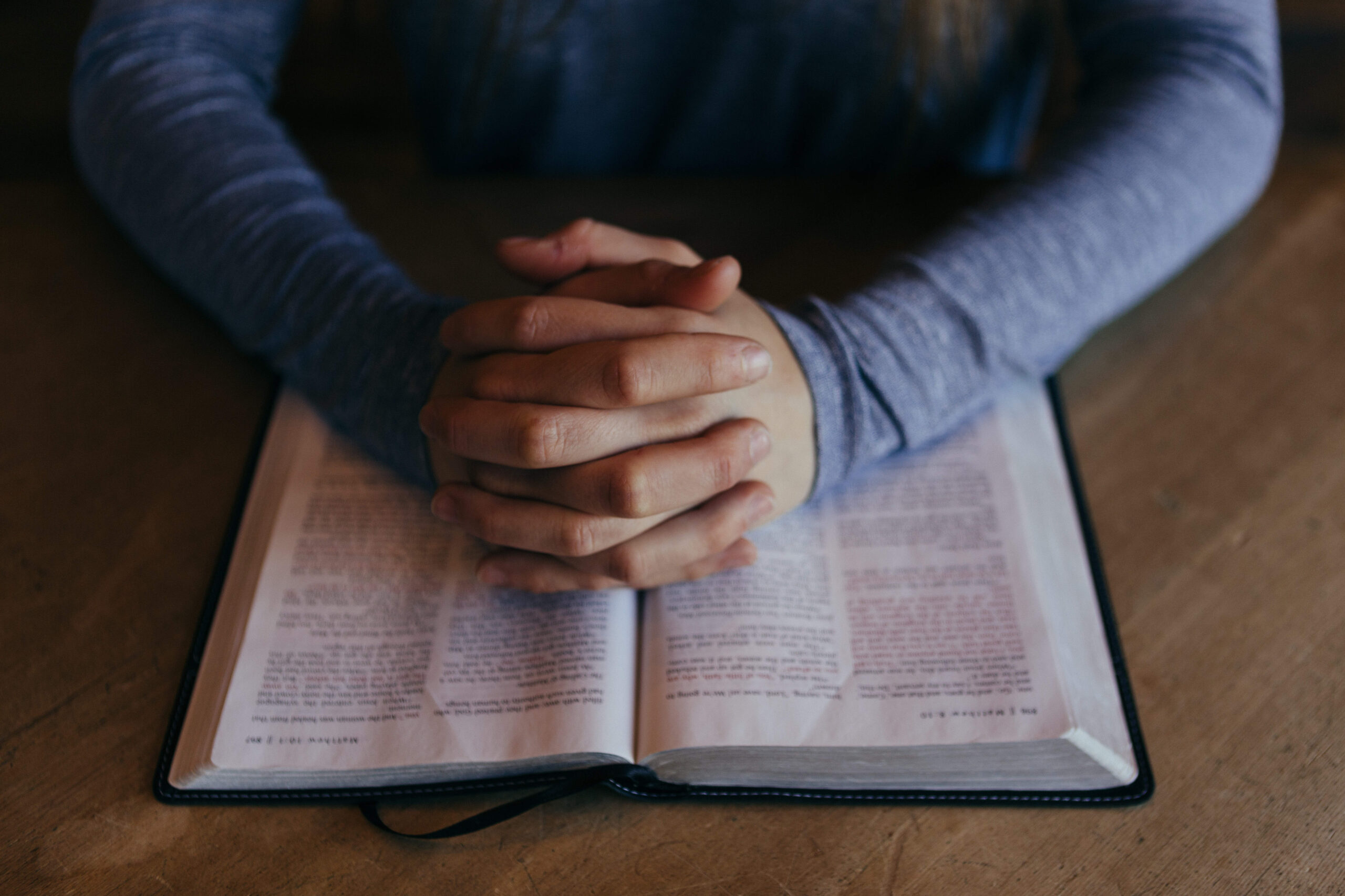 Hands joined in prayer over an open Bible